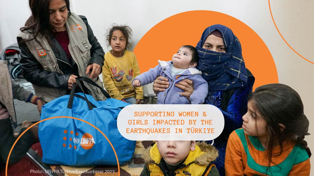 A woman wearing a headscarf sits, holding a baby. Other children are around her as well as a woman in a UNFPA vest.