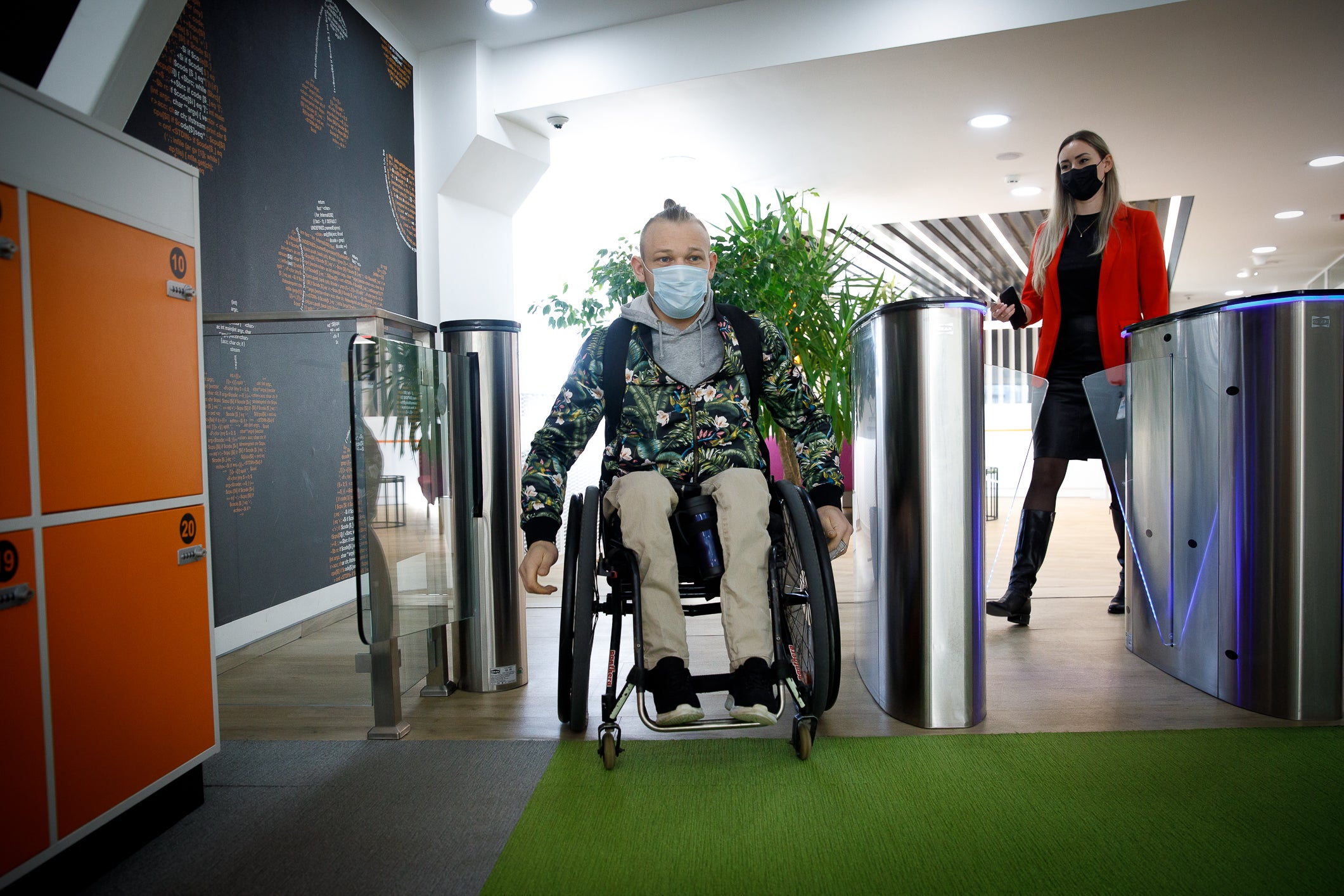 A man using a wheelchair enters his workplace. A woman is seen walking in behind him. 