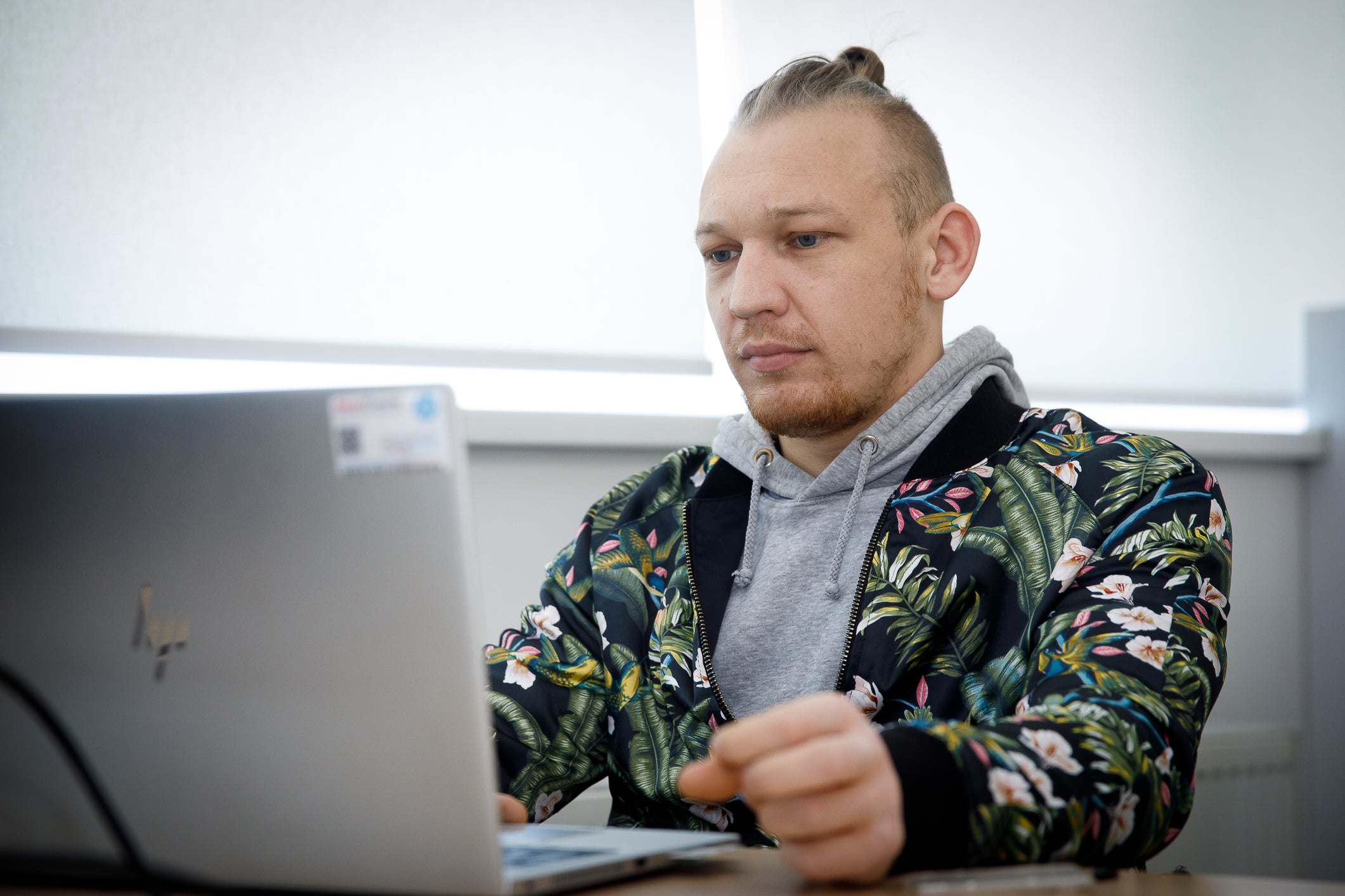 A man with blonde hair and a colorful shirt looks at his laptop screen