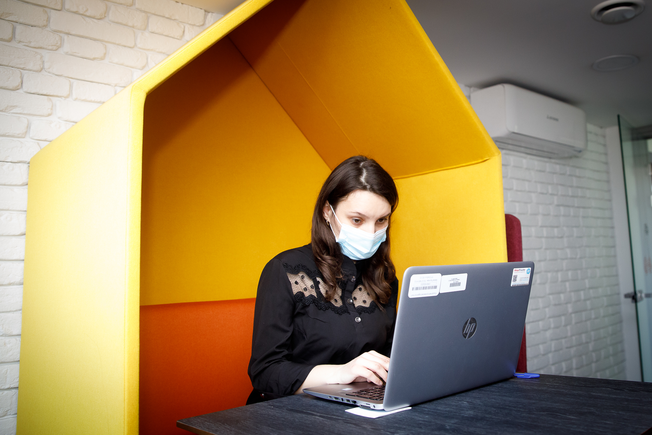 A woman in a black shirt wears a protective face mask and works at a laptop.