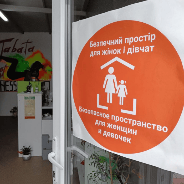 Sign on door with orange UNFPA logo for Women and Girls Safe Space showing stick figure of woman and girl under a roof