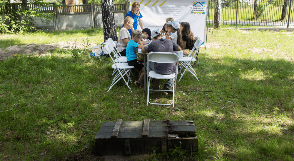 A group of children play around a table outdoors while a leftover box of Russian munitions lays next to them