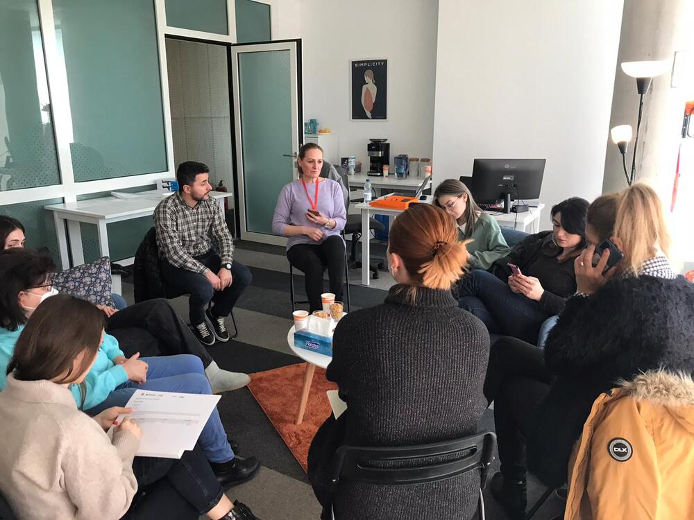 Group of women and one man sit in chairs in a small circle inside an office room