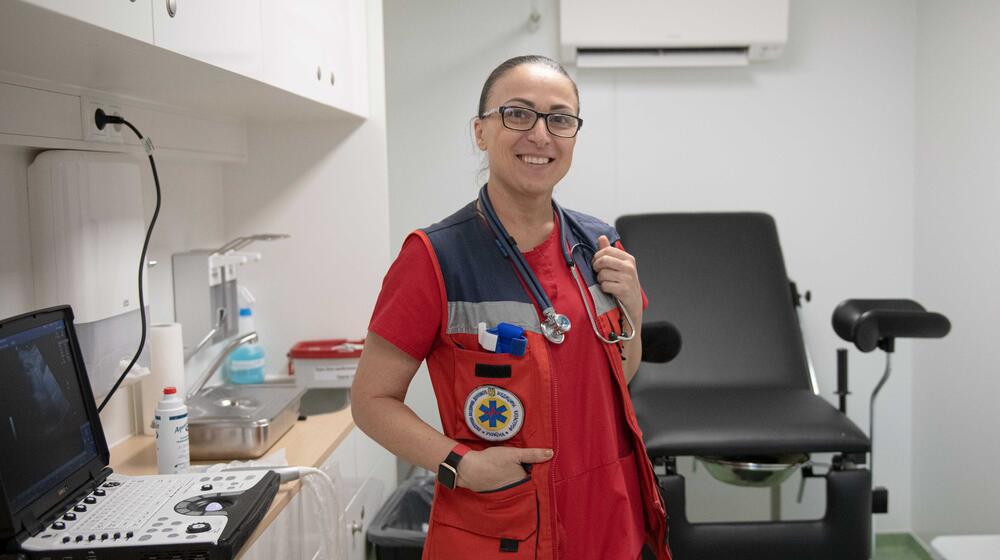 A woman in a red medical outfit stands in a doctor's examination room