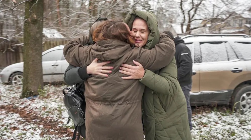 A group of women wearing winter clothes hug outside, in a cold environment.