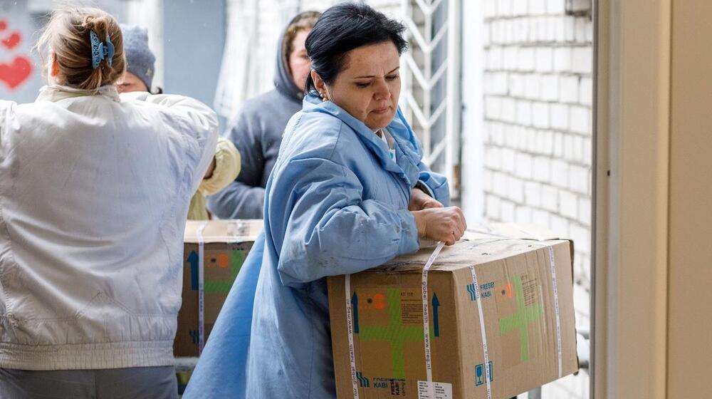 A woman in a medical lab coat opens a box of supplies