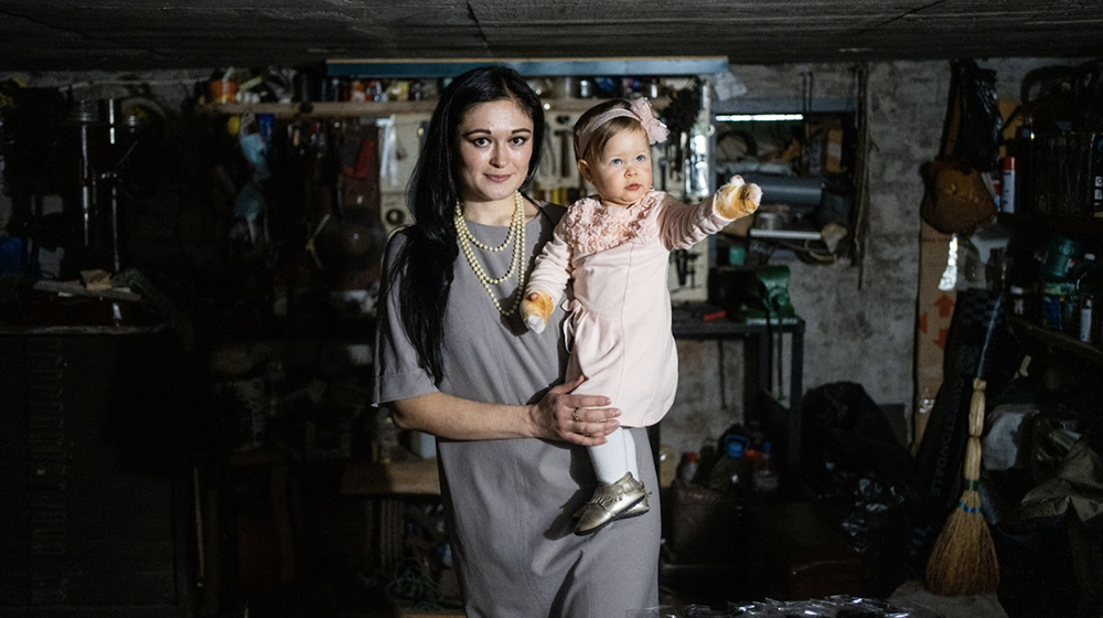 A mother stands in a basement holding a baby girl. 