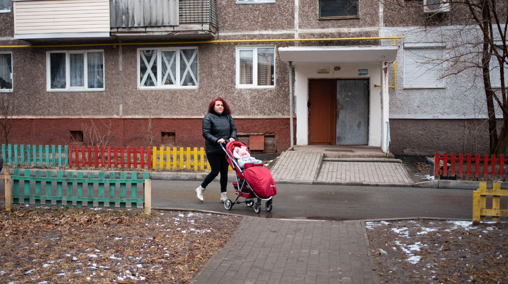A woman pushing a baby in a stroller outside of an apartment building.