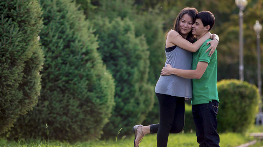 A young man and woman embrace in a green space