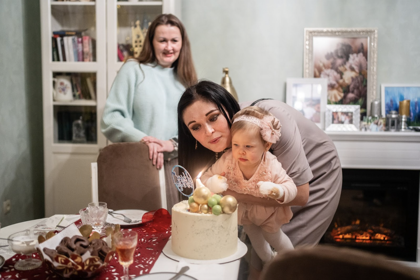 A woman holds her baby over a birthday cake and helps the baby blow the candles out.