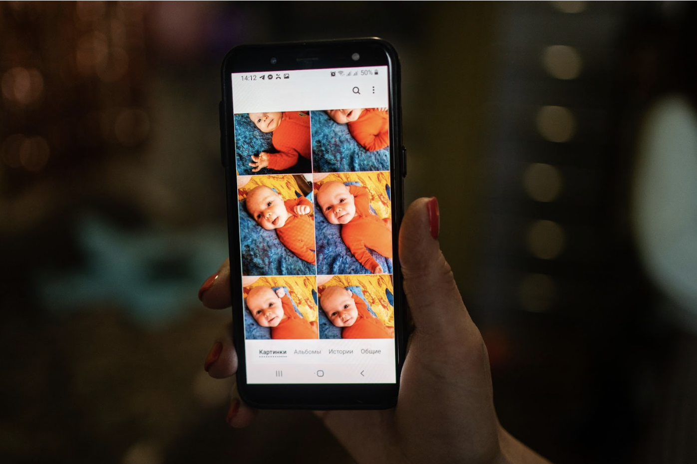 A hand holding a cell phone. On the phone screen there are photos of babies.