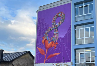 A blue and white building is shown with a large purple mural painted on the side. The mural has a flower with an 8 inside of it.