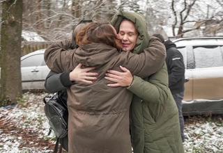 A group of women wearing winter clothes hug outside, in a cold environment.