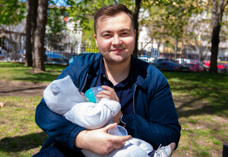 A young father is sitting on a bench in a park in Moldova holding his baby 