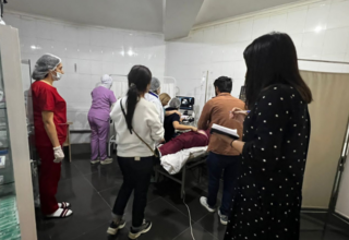 Group of health care workers in a hospital room gather around to observe a woman having an ultrasound