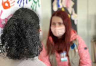 Two women talking together. One with her back to the camera, the other wearing a mask.