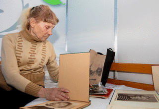 An older woman in a tan sweater looks through a photo album
