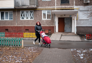A woman pushing a baby in a stroller outside of an apartment building.