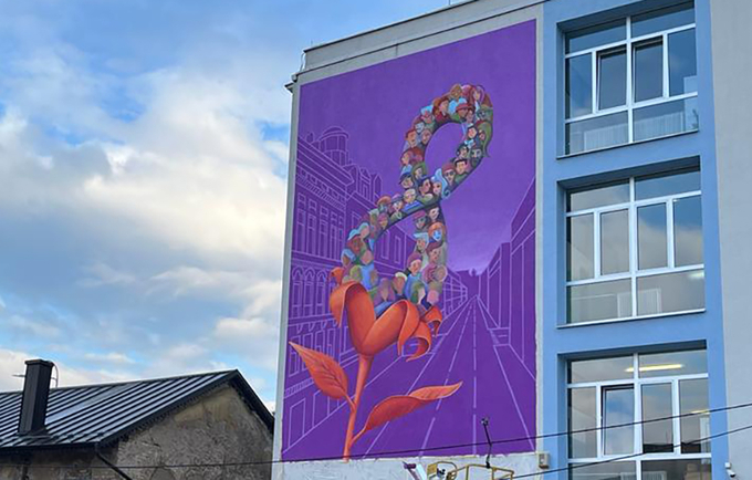 A blue and white building is shown with a large purple mural painted on the side. The mural has a flower with an 8 inside of it.