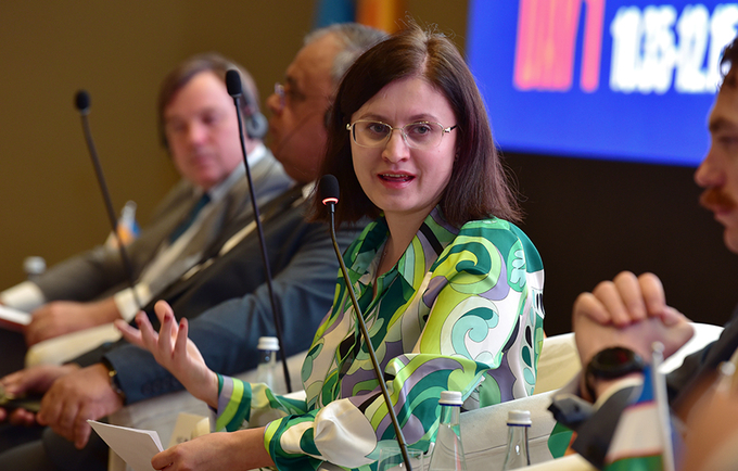 A woman wearing glasses and a green shirt speaks on a panel discussion.