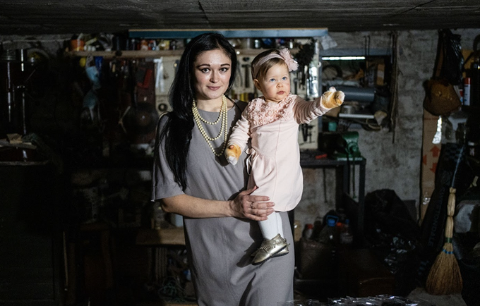 A mother stands in a basement holding a baby girl. 