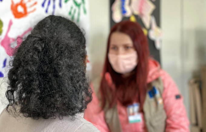 Two women talking together. One with her back to the camera, the other wearing a mask.