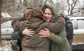 A group of 3 women hug. They are outdoors and there is snow in the background.