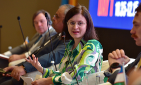 A woman wearing glasses and a green shirt speaks on a panel discussion.