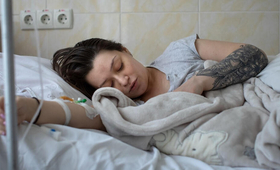 A woman lays in a hospital bed with her eyes closed. Next to her is a blanket wrapped up around a baby.