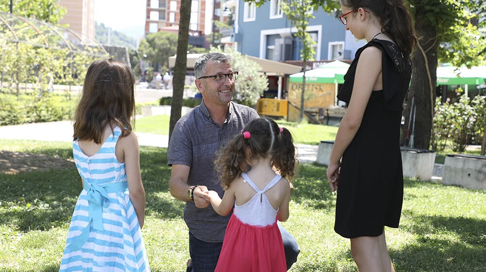 A father kneels in the grass while playing with his three daughters