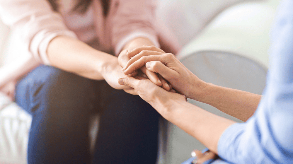 Close up photo of two women holding hands in a supportive and comforting manner