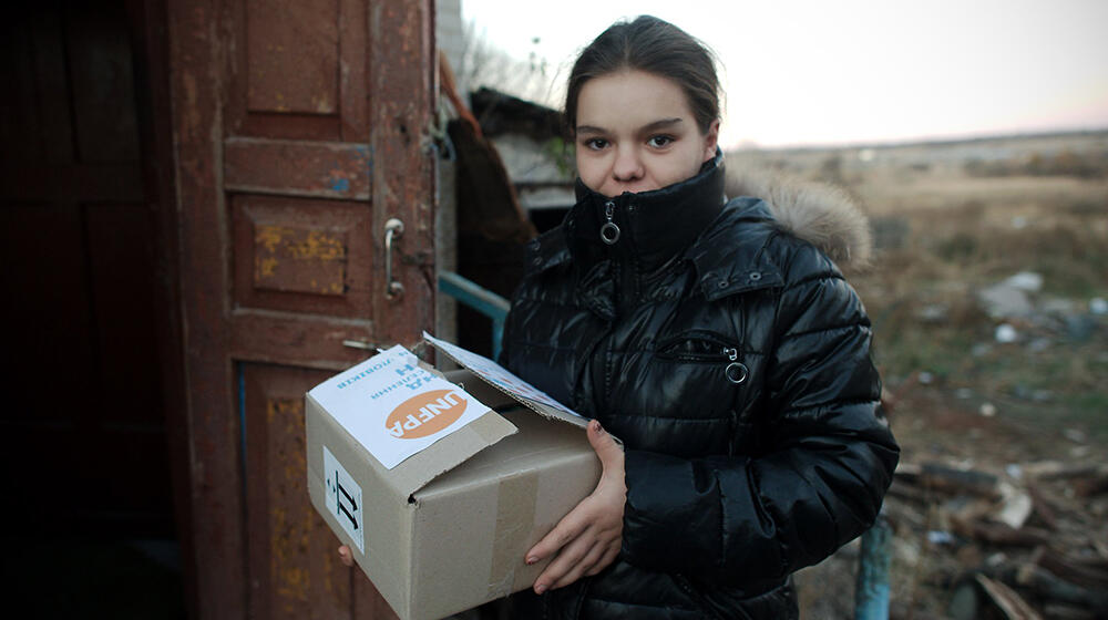 A young woman stands holding a UNFPA box