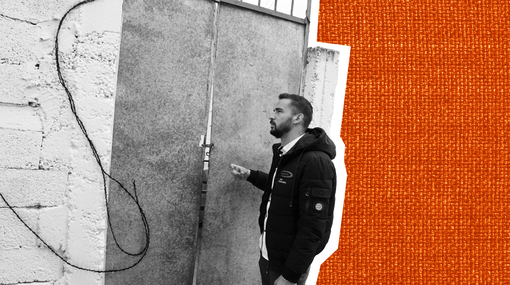 A black and white photo of a man knocking on a large gate door.