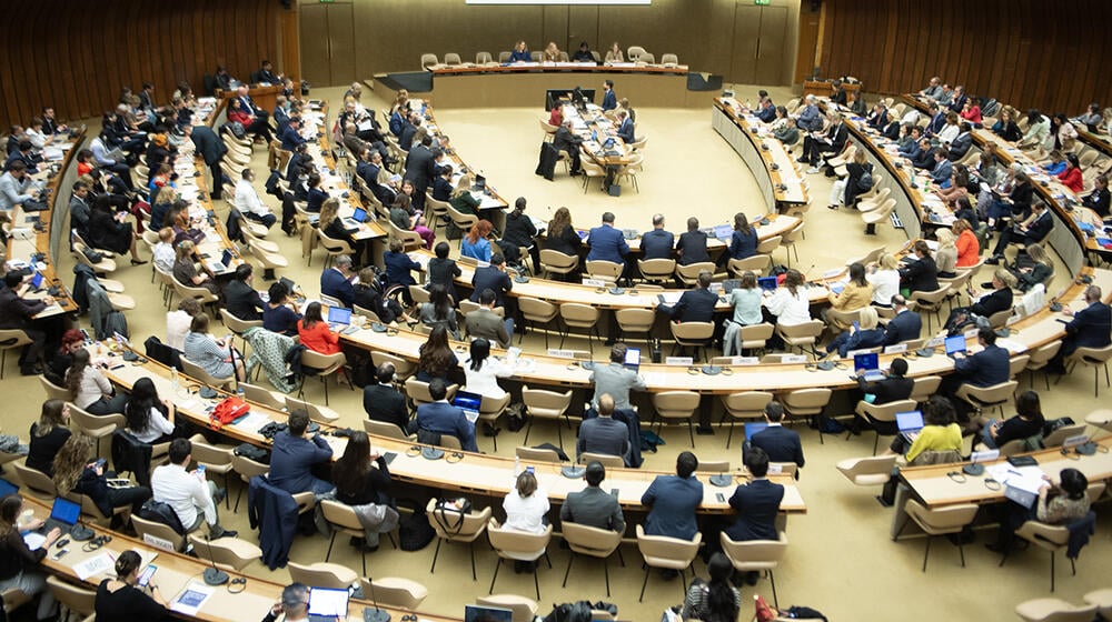 A large conference room set up in a semi-circle and photographed from above. There are many delegates seated.