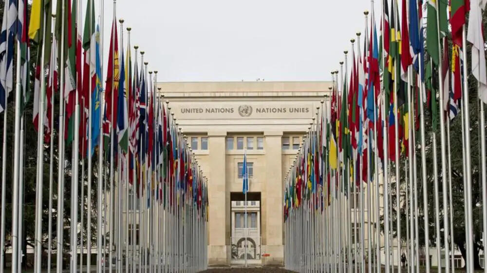 Photograph of the exterior of the United Nations building in Geneva with two rows of flags.