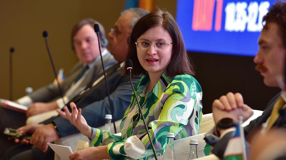 A woman wearing glasses and a green shirt speaks on a panel discussion.