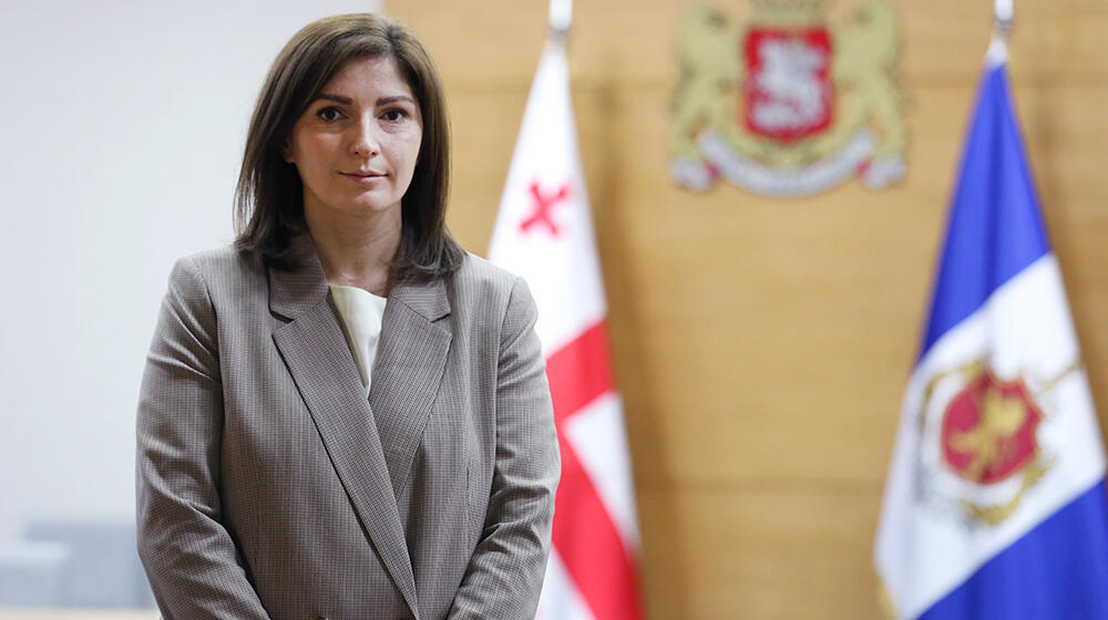 A woman stands in front of two flags