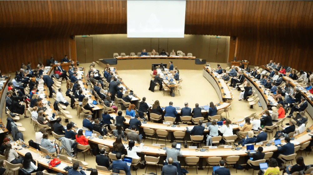 A large conference room set up in a semi-circle and photographed from above. There are many delegates seated.