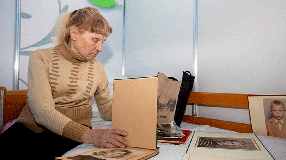 An older woman in a tan sweater looks through a photo album