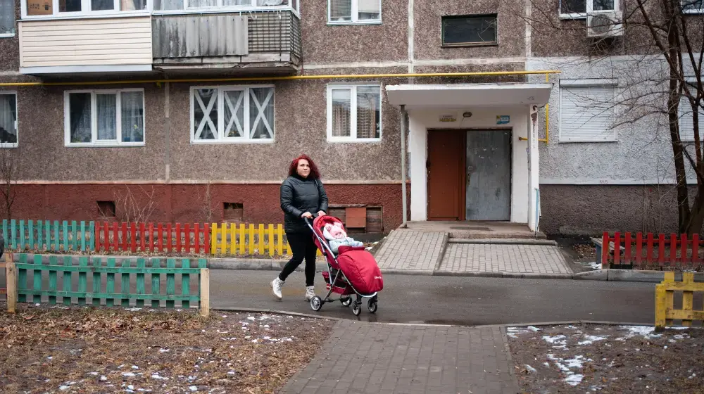 A woman pushing a baby in a stroller outside of an apartment building.