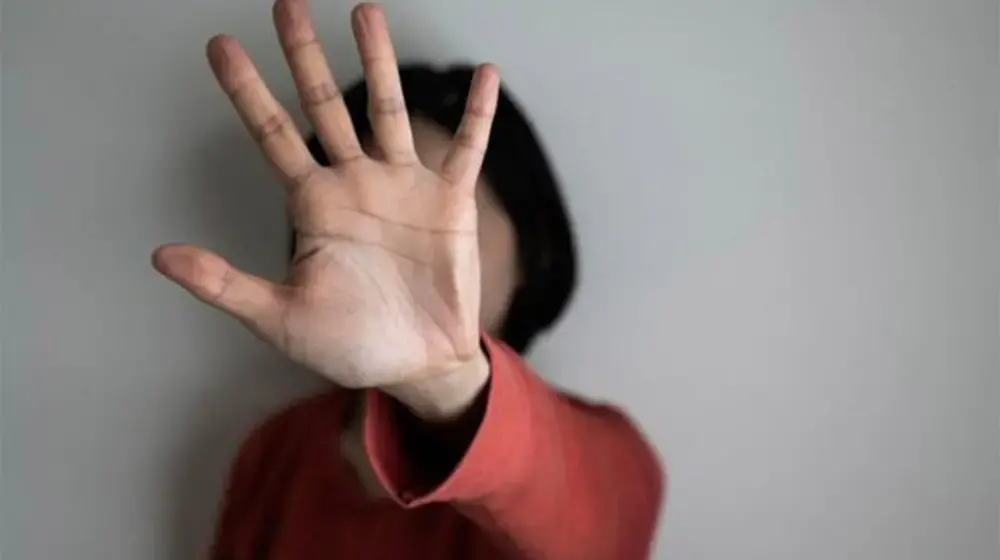 Photo shows a woman, blurred, holding her palm straight out in front of her and obscuring her face. 