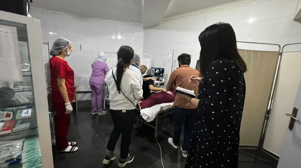 Group of health care workers in a hospital room gather around to observe a woman having an ultrasound