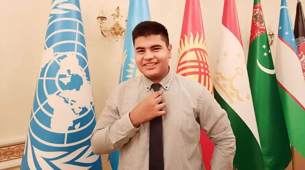 A man standing in front of flags wearing a tie