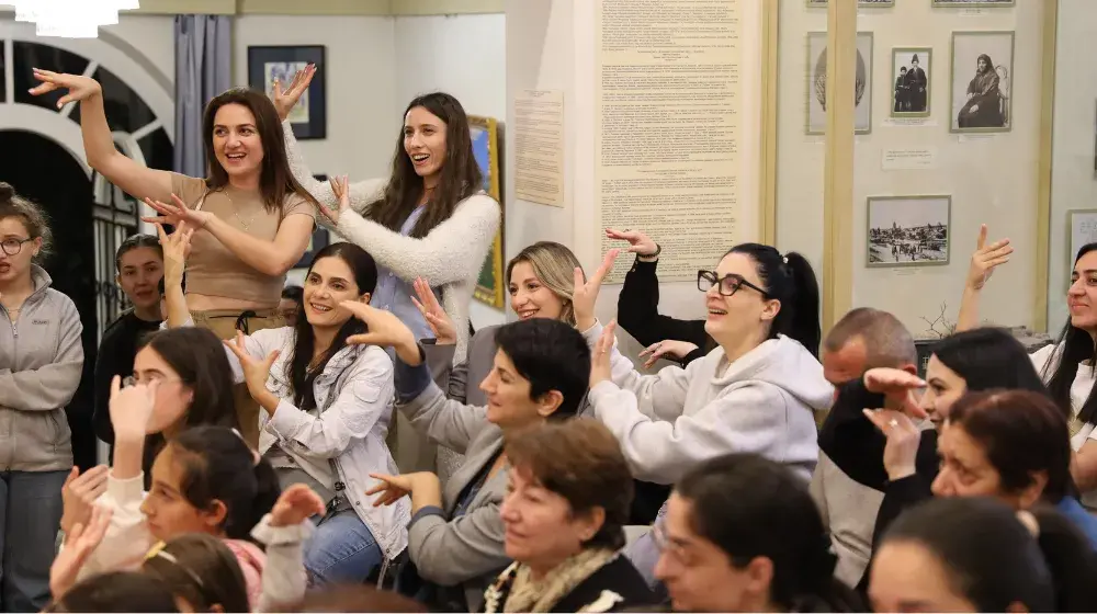 A room full of people who are putting their arms up in the air and communicating with sign lanugage