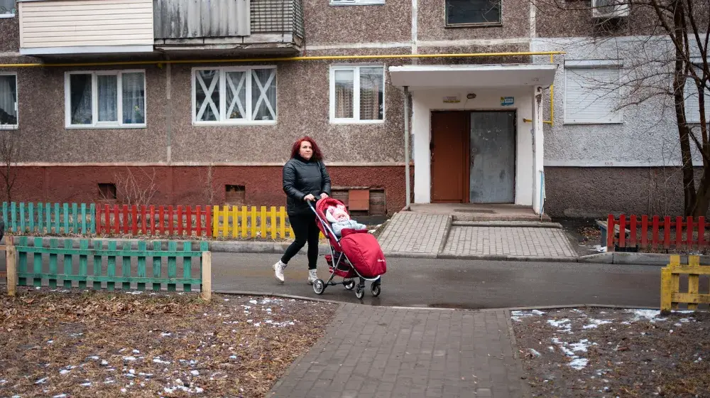 A woman pushing a baby in a stroller outside of an apartment building.