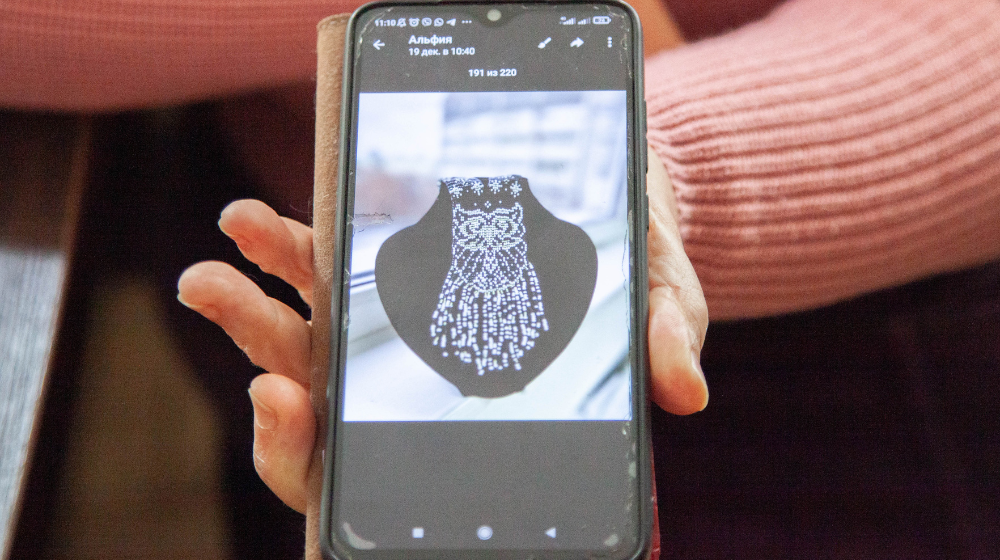 Woman's hand holding a cellphone showing Iryna Harifulina's beaded necklace design