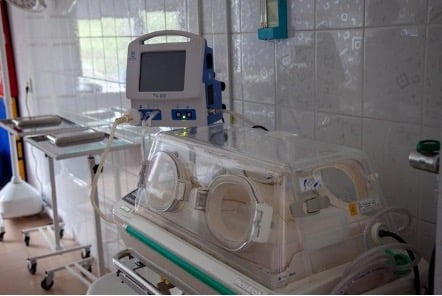 A mobile incubator sits in an empty hospital room next to other medical equipment
