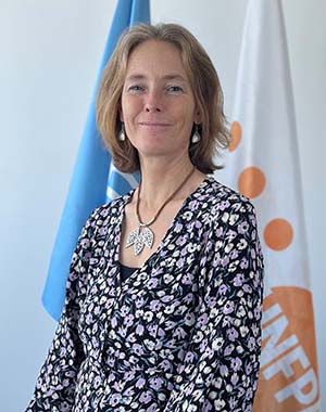 Florence Bauer stands in front of a UN and UNFPA flag, smiling